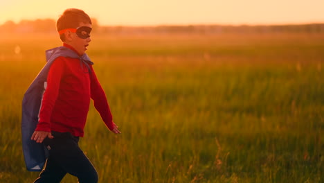 A-boy-in-a-superhero-costume-at-sunset-runs-across-the-field-laughing-and-smiling.